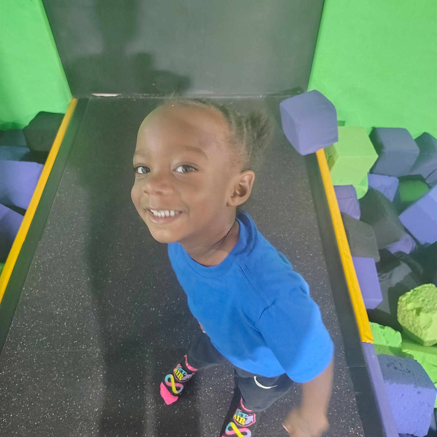 Syere is registered to the contest to win money with this photo: child, smiling, trampoline, foam_blocks, blue_shirt, braided_hair, socks, play, indoor, happy, person, colorful, fun, active, young, feet, floor, background, recreation, casual