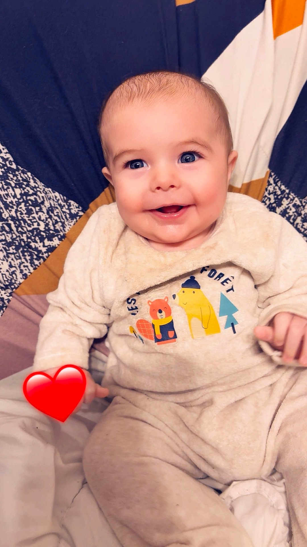 Nao a rejoint le concours — aidez-le/la à gagner de superbes lots ! baby, infant, smiling, blue_eyes, face, onesie, bib, blanket, bed, heart_emoji, pajamas, sitting, indoor, cute, chubby_cheeks, portrait, fabric_pattern, hands, soft_lighting, closeup