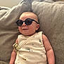 baby, sunglasses, onesie, couch, infant, smiling, indoor, child, cute, relaxed, clothing, seat, young, person, fabric, portrait, comfortable, cozy, casual, home