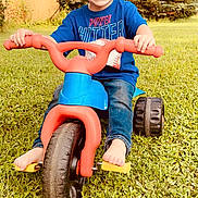 Charleston is registered to the contest to win money with this photo: child, boy, smiling, tricycle, barefoot, grass, outdoor, play, toy, blue_shirt, jeans, greenery, trees, shed, summer, happy, portrait, grass_field, daylight, nature