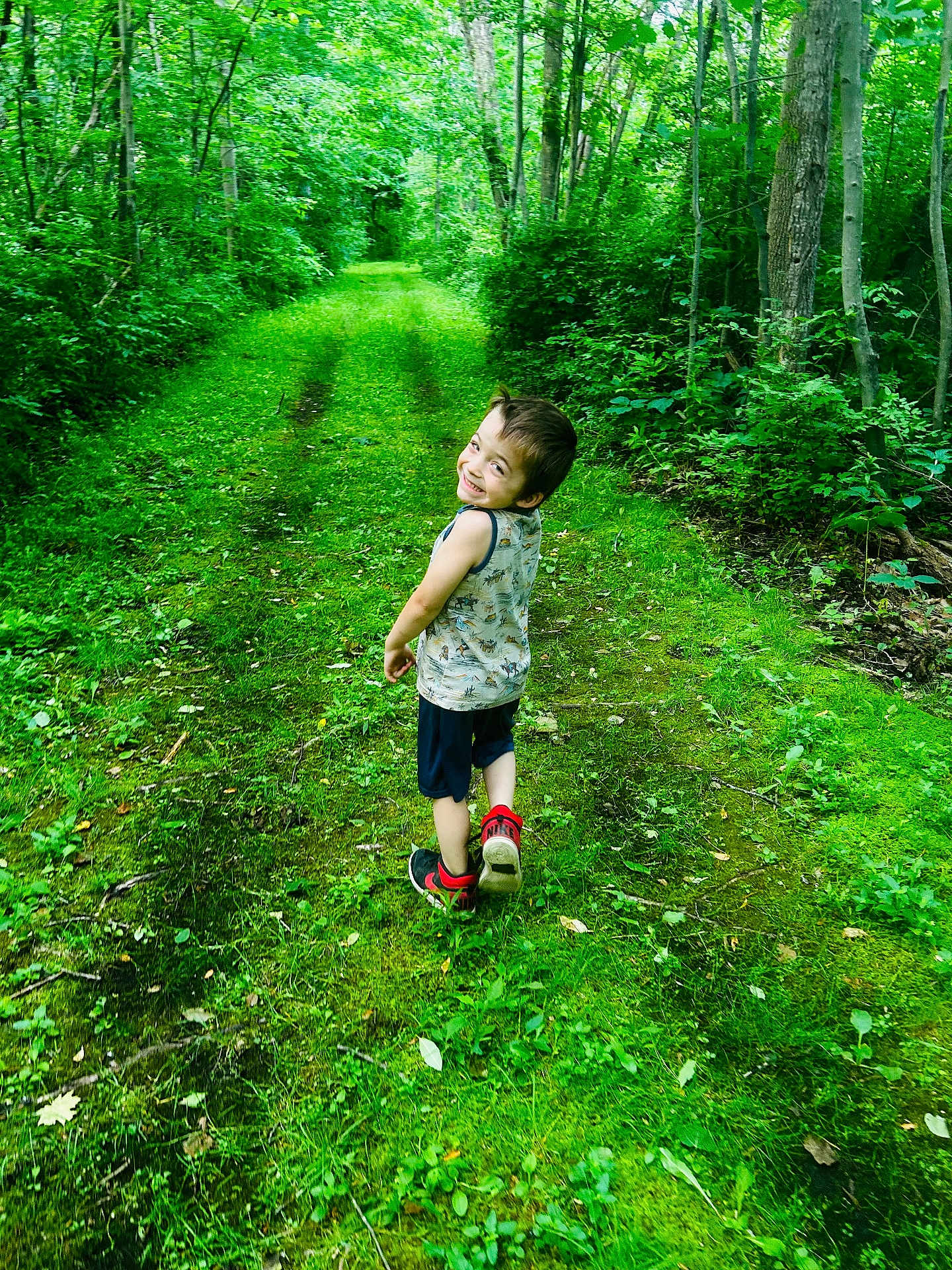 Charleston is registered to the contest to win money with this photo: child, boy, smiling, forest, path, greenery, trees, nature, outdoor, walking, happy, shorts, sneakers, tank_top, grass, summer, young, person, leaves, adventure
