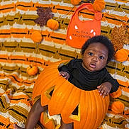 Laiyoni is registered to the contest to win money with this photo: baby, bib, black_clothing, carved_pumpkin, child, crocheted_blanket, cute, decorations, face, feet, festive, halloween, holiday, indoors, infant, legs, orange, portrait, pumpkin, seasonal