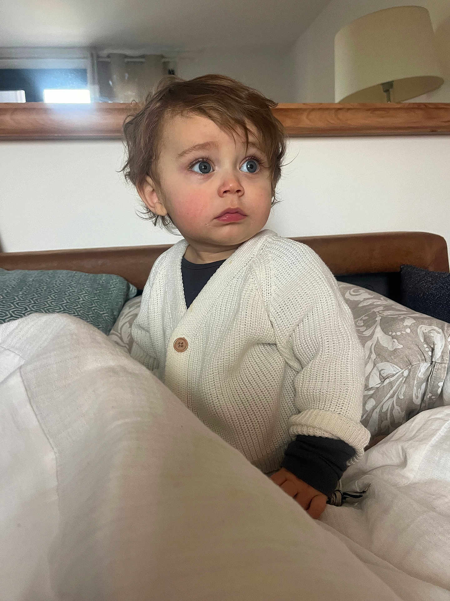 Léon participe au concours pour gagner de l'argent avec cette photo : toddler, child, indoors, portrait, sweater, white, blue_eyes, curly_hair, pillow, blanket, lamp, furniture, home, cozy, cute, sitting, young_child, curious, soft_light, casual