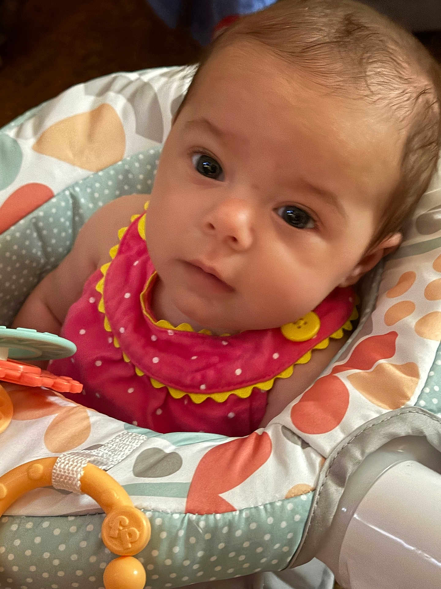 Jocelynn is registered to the contest to win money with this photo: baby, infant, face, eyes, clothing, pink_outfit, yellow_button, baby_seat, polka_dots, toy, closeup, portrait, child, cute, indoor, person, soft_lighting, head, expression, adorable