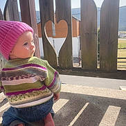 Hazel Anne participe au concours pour gagner de l'argent avec cette photo : child, toddler, baby, pink_beanie, knit_hat, striped_sweater, jeans, bare_feet, wooden_fence, heart_cutout, balcony, outdoors, sunlight, shadow, portrait, side_profile, candid, countryside, railing, concrete_floor