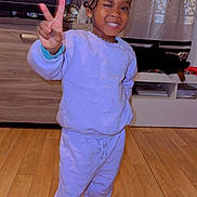 Aminata a rejoint le concours — aidez-le/la à gagner de superbes lots ! child, smiling, winking, peace_sign, pajamas, indoors, wooden_floor, television, curtains, home, person, standing, socks, furniture, cabinet, decor, hair_braids, necklace, earrings, cute