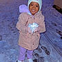 child, snow, winter_clothing, hat, coat, gloves, snowball, footprints, night, outdoor, smiling, person, shoes, street_lights, cold_weather, happy, playful, purple_pants, white_hat, snowy_path