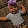 baby, smiling, plaid_couch, purple_headband, flower_accessory, leopard_print_pants, infant, happy, cute, lying_down, indoors, pacifier, child, portrait, clothing, headwear, furniture, patterned, cozy, toddler