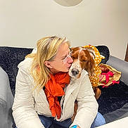 Ravage participe au concours pour gagner de l'argent avec cette photo : woman, dog, kiss, indoor, couch, scarf, white_jacket, orange_scarf, polka_dot_hoodie, brown_dog, glasses, table, cup, black_couch, affection, cozy, casual_clothing, relaxed, pet, friendship
