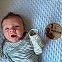 baby, infant, one_month, milestone_marker, striped_clothing, green_clothing, blue_blanket, textured_blanket, spiky_hair, cute, smiling, lying_down, indoors, newborn, portrait, face, hand, person, child, happy