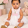 baby, child, portrait, sitting, indoors, pink_dress, white_dress, bow, necklace, shoes, teddy_bear, flowers, bouquet, nursery, carpet, fluffy_rug, studio_photography, curly_hair, smiling, fashion