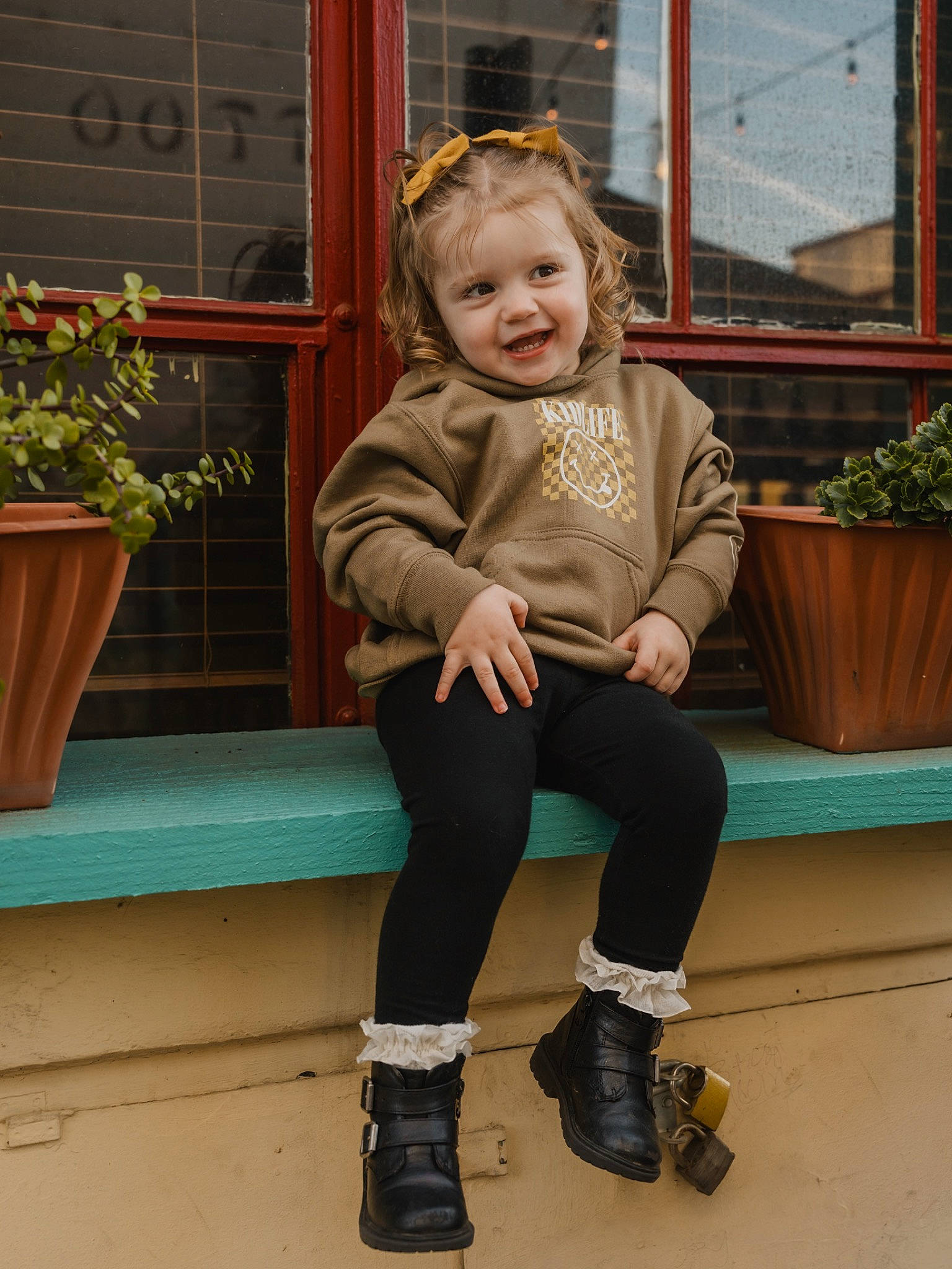 Harleigh is registered to the contest to win money with this photo: baby_toddler_clothing, denim, electric_blue, flower, flowerpot, footwear, houseplant, human_body, human_leg, joint, joy, knee, person, plant, sitting, sleeve, smile, sock, standing, thigh