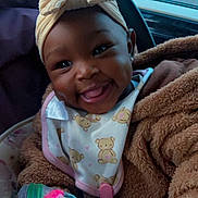 Shiloh is registered to the contest to win money with this photo: baby, smiling, child, car_seat, headwrap, bow, fleece_jacket, bib, toy, hand, indoors, window, car, parking_lot, happy, cute, portrait, face, infant, clothing