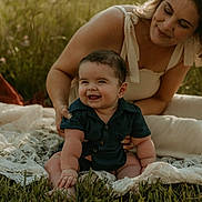 Andrew is registered to the contest to win money with this photo: baby, woman, grass, outdoor, smiling, blanket, lace, sunlight, happy, nature, portrait, child, casual_clothing, sitting, supporting, mother, family, greenery, daylight, cute