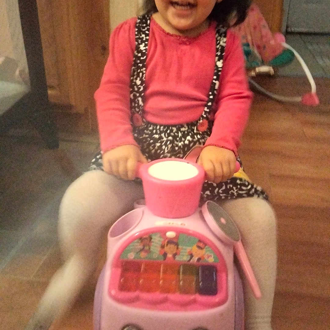 Deanna is registered to the contest to win money with this photo: baby_rocker, child, clothing, cute, face, flooring, fun, furniture, hands, happy, indoor, person, pink_toy, play, room, sitting, smiling, toddler, toy, wooden_floor