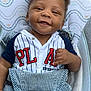 baby, smiling, infant, clothing, striped_shirt, overalls, seat, pattern, hand_gesture, happy, face, cute, child, portrait, indoor, fabric, button, blue, white, red