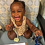 toddler, child, smiling, happy, indoor, chair, keys, lanyard, pacifier, paper, document, clothing, bracelet, hair, face, person, sitting, table, pattern, accessory