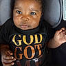 baby, black, car_seat, child, close_up, clothing, cushion, cute, expression, eyes, face, gold_text, hands, indoor, infant, orange_text, person, portrait, shirt, young