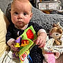 Emmaline is registered to the contest to win money with this photo: baby, child, onesie, fabric_book, plush_toy, blanket, couch, indoor, soft_toys, infant, person, cute, portrait, sitting, cozy, home, furniture, toy, expression, young
