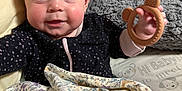 Emmaline is registered to the contest to win money with this photo: baby, infant, blanket, teething_ring, pillow, couch, face, hand, clothing, patterned_fabric, smile, indoor, cute, child, soft_toy, plush, head, person, comfort, cozy