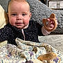 baby, infant, blanket, teething_ring, pillow, couch, face, hand, clothing, patterned_fabric, smile, indoor, cute, child, soft_toy, plush, head, person, comfort, cozy