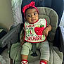 Arya is registered to the contest to win money with this photo: baby, child, high_chair, bib, headband, red_bow, socks, apple, clothing, indoor, portrait, cushion, seat, cute, infant, person, expression, smile, face, comfort