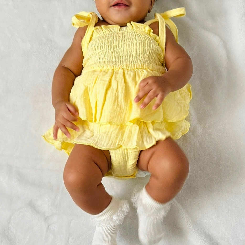 Arya joined the competition — help win amazing prizes! baby, born_2025, child, close_up, cute, hands, happy, headband, indoor, infant, legs, lying_down, portrait, smiling, socks, soft_texture, three_months, white_blanket, wooden_plaque, yellow_dress