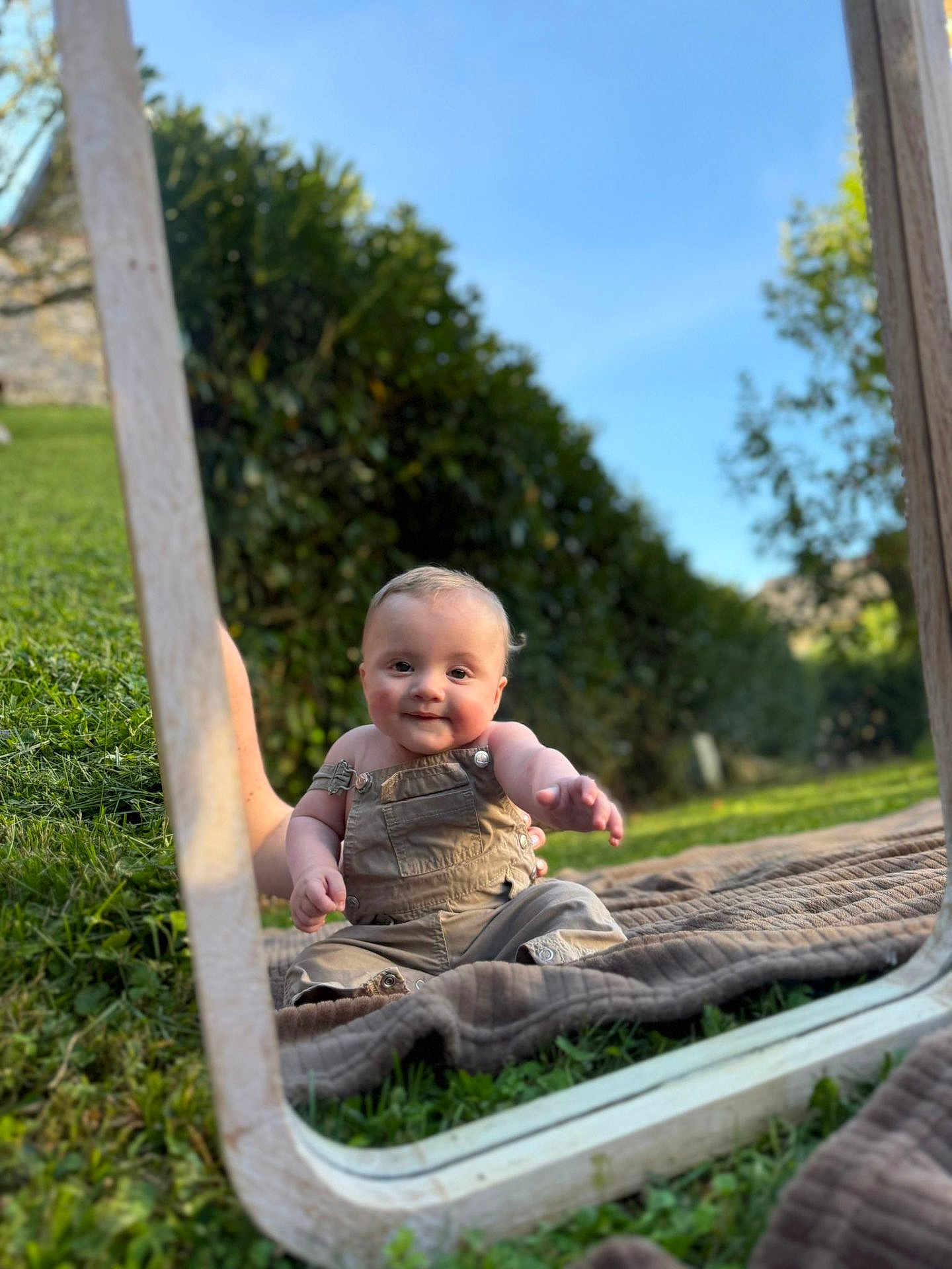 Gabin participe au concours pour gagner de l'argent avec cette photo : baby, child, mirror, reflection, outdoor, grass, blanket, smile, happy, nature, sunny, blue_sky, greenery, overalls, cute, portrait, sitting, daylight, wooden_frame, curious