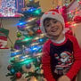 child, christmas_tree, holiday, festive, santa_hat, pajamas, smiling, indoor, decorations, lights, ornaments, red, green, happy, home, celebration, seasonal, young_child, joyful, wall