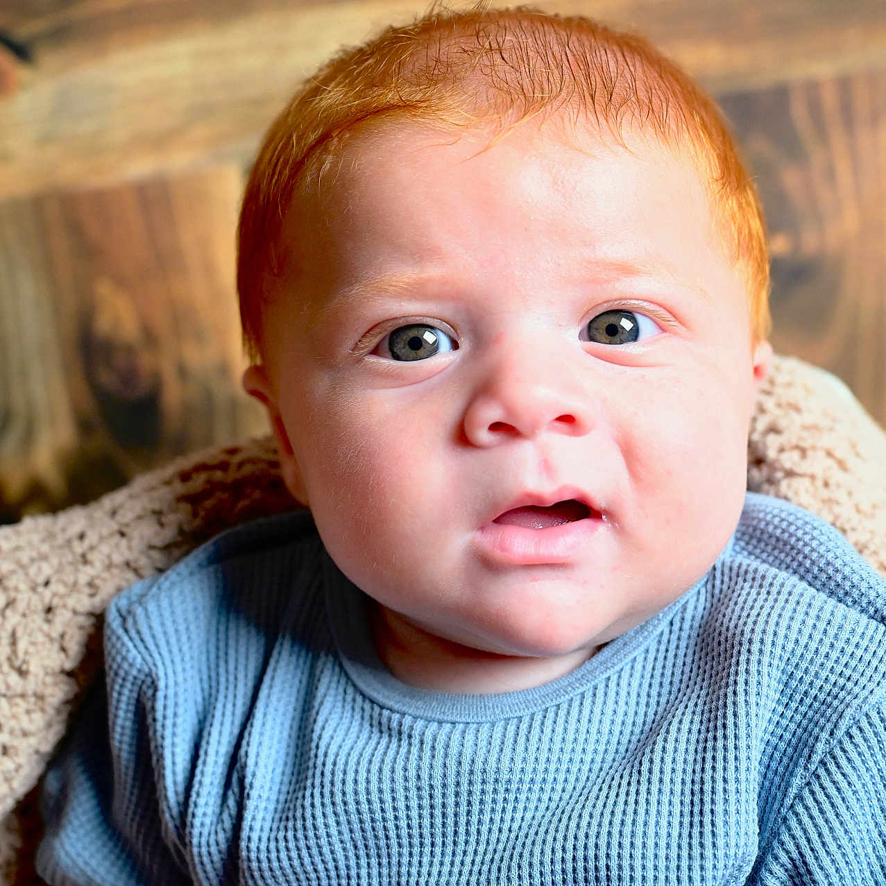 Aaron participe au concours pour gagner de l'argent avec cette photo : baby, blanket, blue_shirt, child, cozy, curious, cute, expression, eyes, face, indoor, infant, person, portrait, red_hair, sitting, skin, soft, wooden_background, young