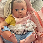 Arabella is registered to the contest to win money with this photo: baby, infant, child, pink_seat, yellow_shirt, blue_pants, bare_feet, blanket, bib, indoors, floor, cushion, person, cute, wide_eyes, soft_toys, comfort, portrait, baby_clothing, holding_leg