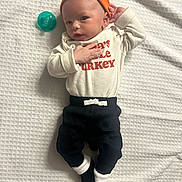Elohim is registered to the contest to win money with this photo: baby, infant, orange_cap, white_blanket, pacifier, clothing, black_pants, socks, cute, portrait, lying_down, child, newborn, small_hands, looking_at_camera, indoor, soft_texture, cozy, casual_wear, adorable