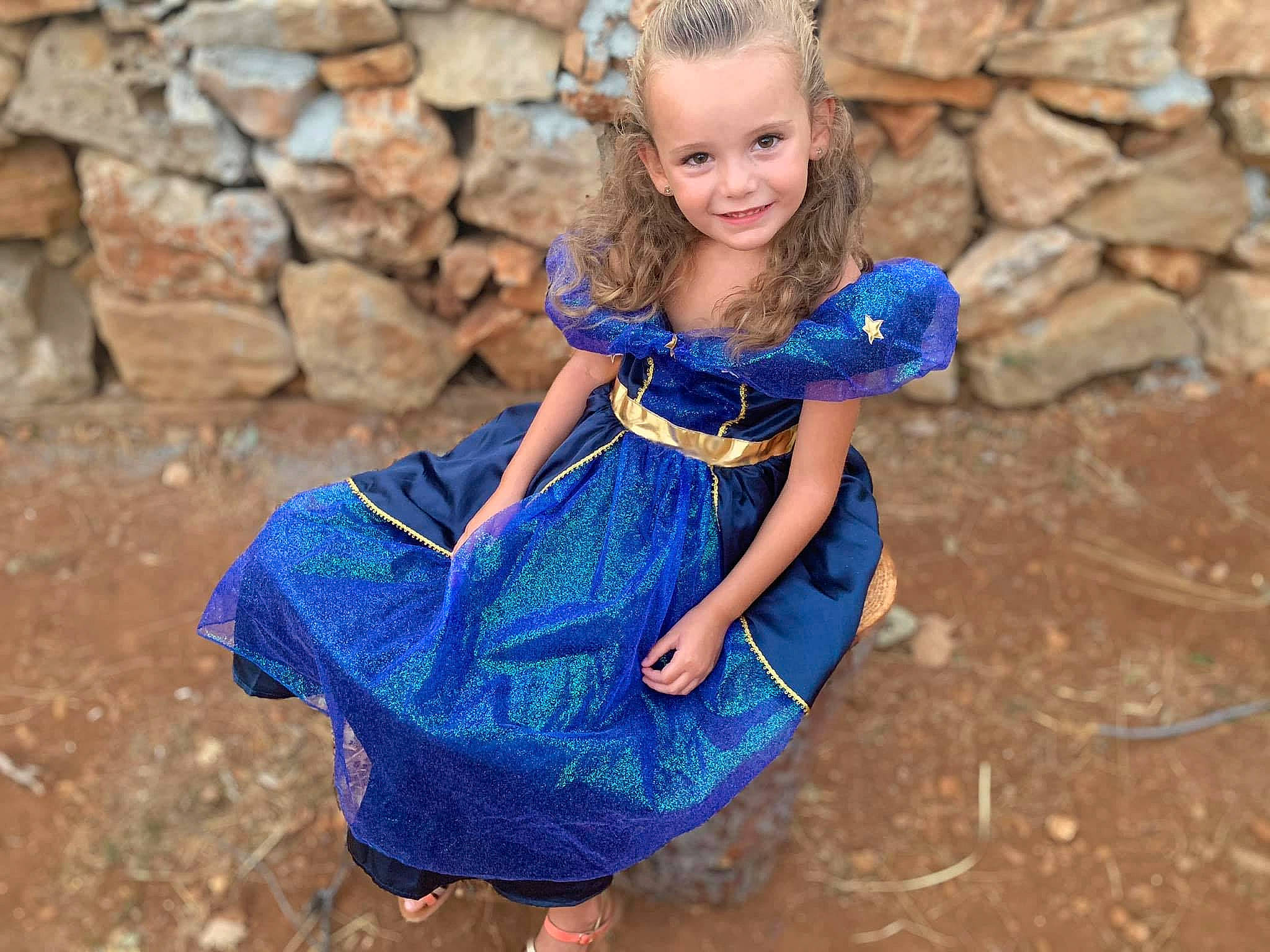 Léna participe au concours pour gagner de l'argent avec cette photo : blond, blue, brick, child_model, costume, day_dress, dress, electric_blue, embellishment, fictional_character, hair_accessory, joy, one_piece_garment, person, stone_wall, toy