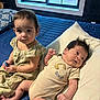 baby, infant, child, bed, pillow, blue_bedspread, window, toy_car, indoor, curious, calm, clothing, person, hair, skin, face, sitting, lying_down, natural_light, room