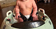 Bobbie joined the competition — help win amazing prizes! baby, baby_toy, cabinet, child, child_seat, curly_hair, cute, diaper, expression, floor, furniture, harness, home, indoor, playful, room, seat, shoes, toy_car, wooden_floor