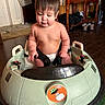 baby, baby_toy, cabinet, child, child_seat, curly_hair, cute, diaper, expression, floor, furniture, harness, home, indoor, playful, room, seat, shoes, toy_car, wooden_floor