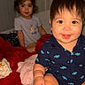 Bobbie is registered to the contest to win money with this photo: baby, bedroom, blanket, blue_shirt, child, clothing, cute, face, hair, happy, hat, indoor, person, red_blanket, sitting, smiling, soft, toddler, toy, wall
