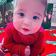 Bobbie is registered to the contest to win money with this photo: baby, infant, red_clothing, close_up, face, hands, holiday, christmas, blanket, indoor, cute, child, portrait, festive, decorations, smiling, young, person, cozy, warm