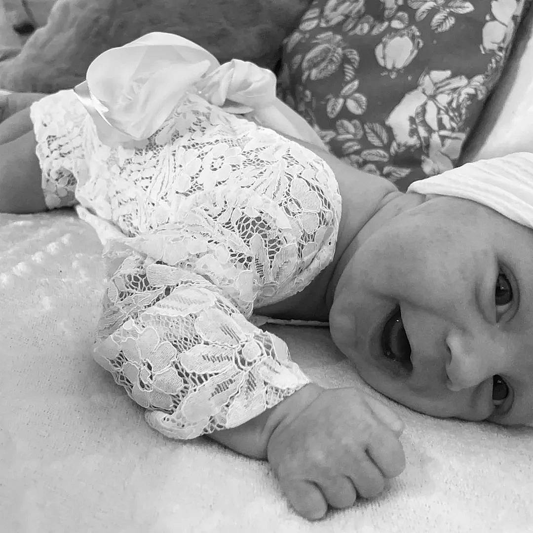 Mia participe au concours pour gagner de l'argent avec cette photo : baby, baby_toddler_clothing, black_and_white, child, comfort, elbow, flooring, gesture, grey, happy, headwear, human_body, human_leg, monochrome, monochrome_photography, person, sleeve, smile, style, textile