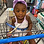 Cecelia is registered to the contest to win money with this photo: baby, child, shopping_cart, headband, toy, store_aisle, shopping, retail, clothing, footwear, person, cute, infant, sitting, beads, purple, curious, indoor, supermarket, safety_belt