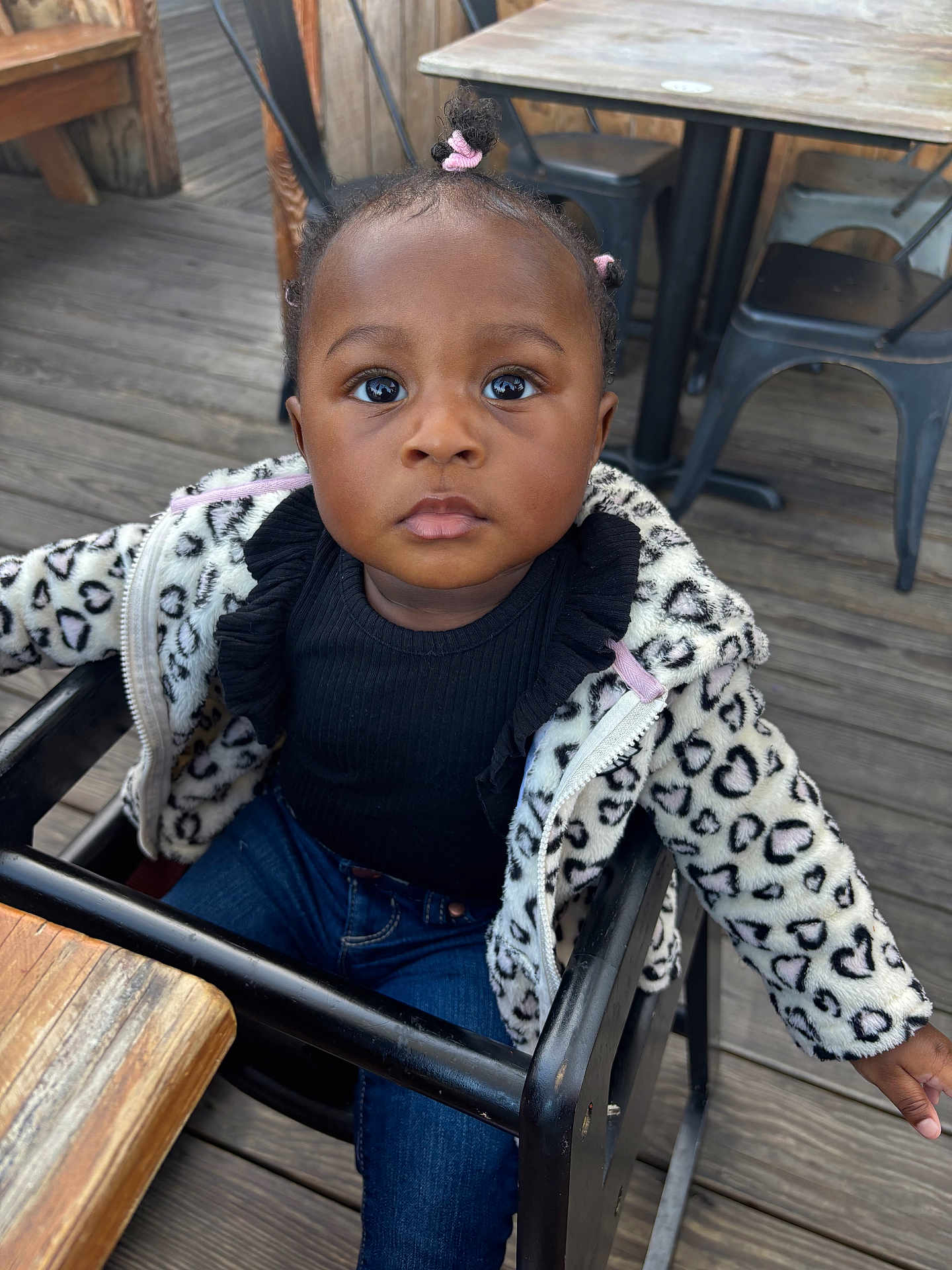 Cecelia joined the competition — help win amazing prizes! toddler, child, high_chair, jacket, heart_pattern, pink_hair_ties, jeans, wooden_floor, metal_chairs, curious_expression, outdoor, portrait, clothing, person, seat, table, black_top, baby, cute, young_child