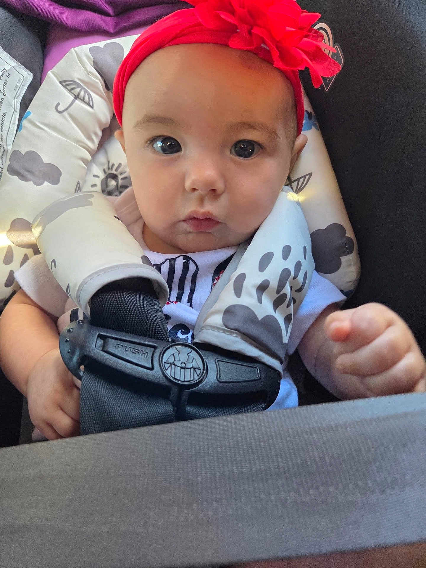 Ariella is registered to the contest to win money with this photo: baby, child, infant, headband, red_flower, car_seat, harness, seatbelt, closeup, face, eyes, hands, clothing, patterned, sitting, portrait, cute, indoors, person, young