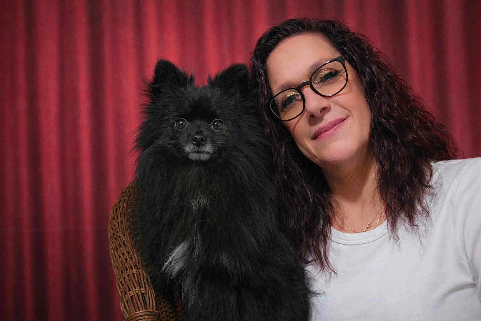 Veilko a rejoint le concours — aidez-le/la à gagner de superbes lots ! dog, woman, glasses, portrait, indoor, red_curtain, smile, black_dog, long_hair, wicker_chair, white_shirt, furniture, pet, companion, friendly, face, sitting, curly_hair, domestic_animal, casual