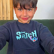 Giulian participe au concours pour gagner de l'argent avec cette photo : child, boy, smiling, sweatshirt, disney, stitch, brown_eyes, brown_hair, indoor, couch, wood, casual_clothing, portrait, happy, young, person, seated, furniture, cute, playful