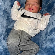 London is registered to the contest to win money with this photo: baby, newborn, sleeping, infant, white_sweatshirt, nike_logo, grey_pants, blue_blanket, soft_texture, cozy, cute, peaceful, hands, face, head, clothing, footed_pants, portrait, lying_down, indoor