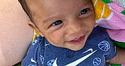 London is registered to the contest to win money with this photo: baby, child, smiling, outdoor, grass, towel, blue_clothing, sportswear, basketball, baseball, soccer_ball, happy, face, infant, cute, person, closeup, head, skin, sunlight