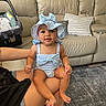 Leilani is registered to the contest to win money with this photo: baby, child, person, indoor, living_room, couch, pillow, blue_outfit, hat, bow, smile, sitting, car_seat, floor, rug, arm, skin, happy, cute, casual