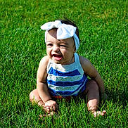 Leilani joined the competition — help win amazing prizes! baby, child, grass, outdoor, smiling, headband, bow, cute, happy, sitting, sunlight, green, nature, one_person, infant, portrait, summer, casual_clothing, playful, young