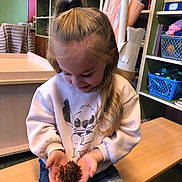 Azëlia participe au concours pour gagner de l'argent avec cette photo : child, girl, sweatshirt, cartoon_character, jeans, bench, indoor, sitting, holding_object, spiky_object, long_hair, pony_tail, shelves, basket, wooden_furniture, curiosity, casual_clothing, room, young, portrait