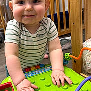 Jayce joined the competition — help win amazing prizes! toddler, child, toy, green_toy, smiling, indoor, nursery, crib, baby, playtime, curious, striped_shirt, hands, wooden_furniture, floor, cute, person, infant, play, happy